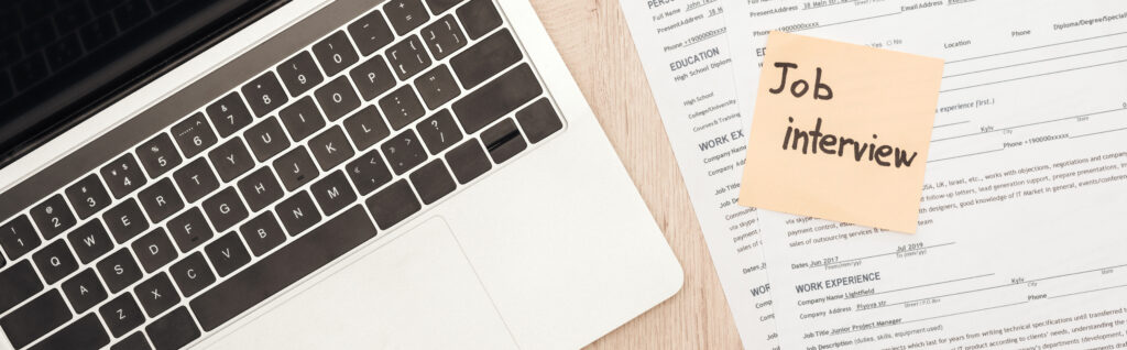 panoramic shot of laptop, resume templates and sticky note with job interview lettering on wooden table