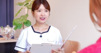 クリップボードを持って笑顔で話す受付スタッフ