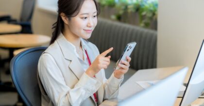 パソコンの前でスマートフォンを操作する女性
